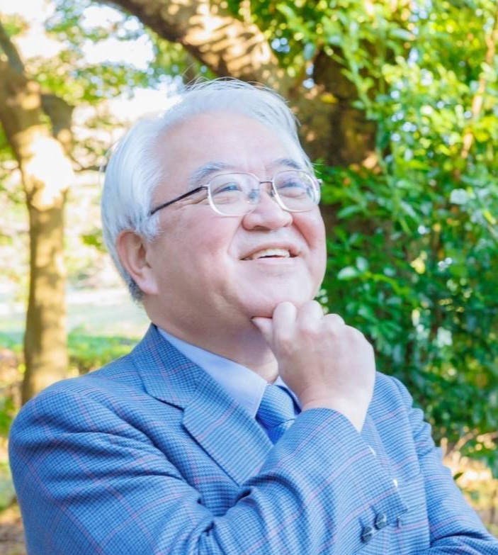 木々を背に、笑顔で遠くを見つめる一般社団法人ちいきん会代表理事の新田信行氏