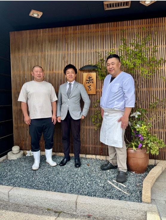 支援先の飲食店の前で、経営者とスタッフとともに並ぶ河村裕司さん